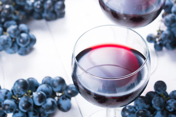 two glasses of red wine and blue grapes on white wooden table background