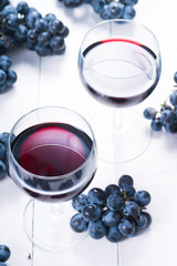two glasses of red wine and blue grapes on white wooden table background