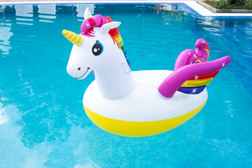 Unicorn pool float in blue water background, inflatable swim tube. Pool party, summer holidays,...