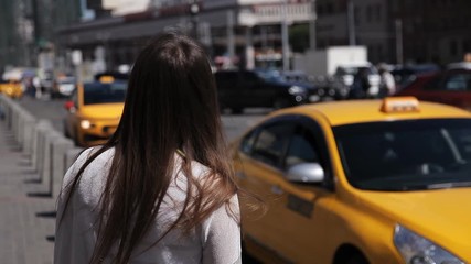 Attractive woman admires the city, yellow taxis pass by.