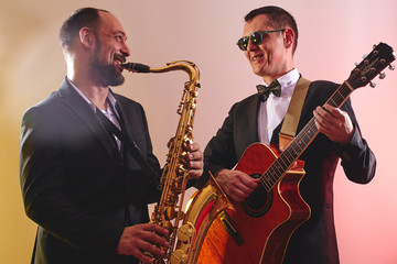Group of two musicians, male jazz band, guitarist and saxophonist in classical costumes improvise...