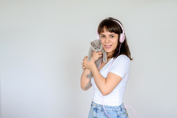 close up photo of a happy brunette with pink headphones listening to the music while holding a gray kitten in her arms