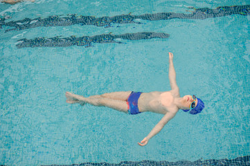top view of a 7-year boy swimming backstroke in a swimming pool