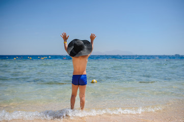 back view photo of a 7-year boy on the beach looking at the sea