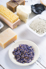 spa products: black mud and clay powder, cosmetic cream, soap, bath salt, shea butter and lavenders on white wood table background