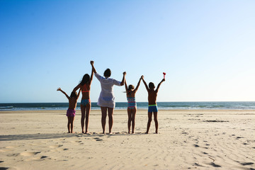 Happy young family on the sunset at the beach. Lifestyle. Single mother on vacation with her children on the beach. Raised arms in height.