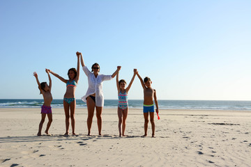 Single mother on vacation with her children on the beach. Raised arms in height. Front view.