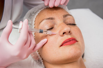 The doctor cosmetologist makes the facial injections procedure. Young woman in a beauty salon.