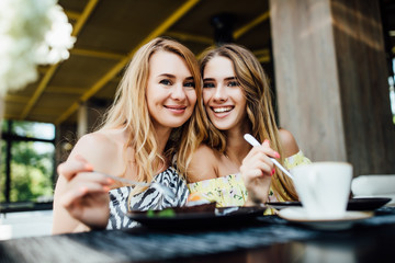 Portrait of two blonde sisters have a breakfast in modern cafe, spend time together.