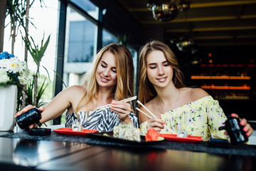 Fototapeta premium Lunch at a Chinese restaurant on the summer terrace. Mom and her young beautiful daughter eat sushi with chinese sticks. Lifestyle.