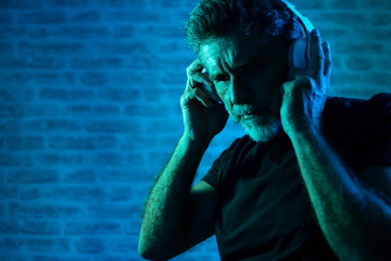 Dark neon portrait of senior man with beard, headphones. party, holidays, celebration, nightlife...