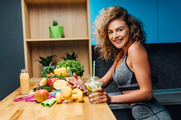 Young woman wearing  top enjoying healthy breakfast, eating fruits, smiling, home kitchen time. Use phone for count calories.