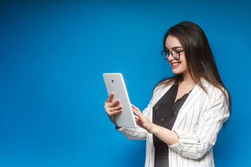 Portrait of a cute young business woman or consultant with laptop speak with someone in blue studio.
