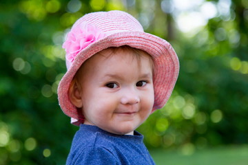 Closeup of adorable fair smiling toddler girl wearing a pink straw hat looking sideways with cheeky expression