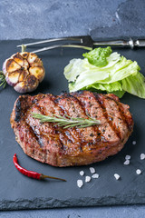 The ribeye steak with sprig of rosemary on a black stone slab
