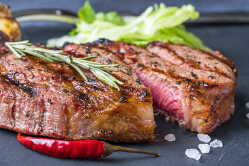 The macro of cutted ribeye steak with sprig of rosemary on a black stone slab