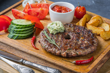 A Slovak meat dishe is on wooden board with tomatoes and fried potatoes