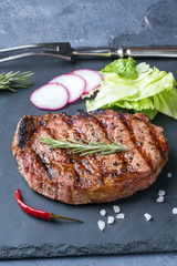 The ribeye steak with sprig of rosemary on a black stone slab