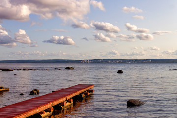 Fototapeta premium Water landscape with a wooden pier on a background of blue sky with white clouds