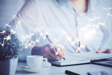 Double exposure of man's hands writing notes of stock market with forex chart.