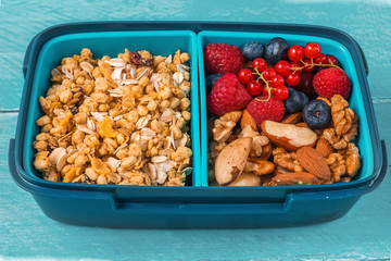 Healthy school lunch box with granola, nuts and berries to make healthy breakfast on blue wooden background