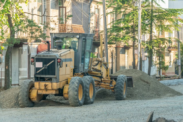 Yellow tractor with a bucket is about a pile of sand. Concept of road and construction works