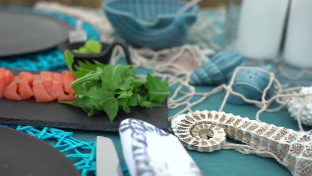 Sea style dining table outdoors with close up of glass of wine, caprese salad, shrimp, oysters and candles camera panning left