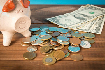 Piggy Bank and a few coins and dollar bills on the wooden table. Close up. The concept of saving money. Selective focus.