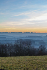 wide angle view of a frosty field and a foggy valley with an Austrian  mountain range in the background