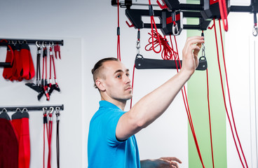 Physiotherapy. Suspension training therapy. Young man doing fitness traction therapy with...