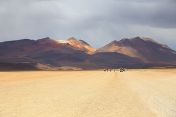 Bolivian desert with arid and dusty soil. Off road adventure in the Andean Highlands. Rally on dusty trails. Cloudy sky and mountains.