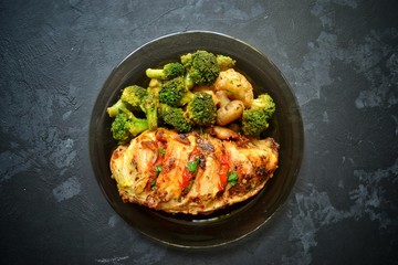 Obraz na płótnie Canvas Fried chicken fillet. Broccoli and cauliflower. Baked chicken breast. Chicken and tomato. Food in a black plate on a black concrete table background.