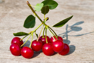 Sprig of ripe red cherry with green leaves on an old wooden table, rustic style, copy space