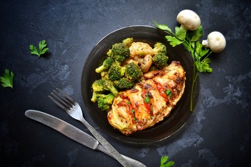 Fried chicken fillet. Broccoli and cauliflower. Baked chicken breast. Chicken and tomato. Food in a black plate on a black concrete table background.