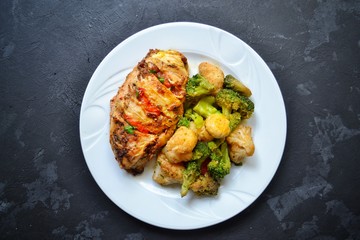 Fried chicken fillet. Broccoli and cauliflower. Baked chicken breast. Chicken and tomato. Food in a white plate on a black concrete table background.