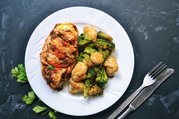 Fried chicken fillet. Broccoli and cauliflower. Baked chicken breast. Chicken and tomato. Food in a white plate on a black concrete table background.