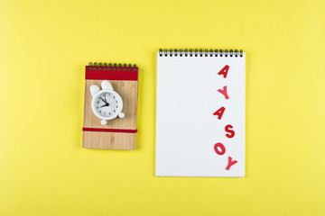 Back to school mockup concept. Notepad, pencil, alarm clock on yellow background. Flat lay, top view, copy space