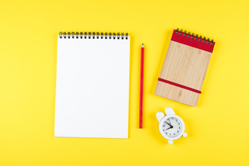 Back to school mockup concept. School time minimal concept. Notepad, pencil, alarm clock on yellow paper background. Flat lay, top view, copy space