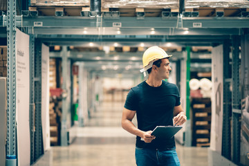 Smart Indian engineer man worker wearing safety helmet doing stocktaking of product management in cardboard box on shelves in warehouse. Factory physical inventory count.