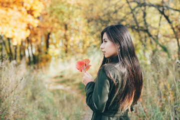 Naklejka premium Female beauty portrait surrounded by vivid foliage. Dreamy beautiful girl with long natural black hair on autumn background with colorful leaves in bokeh. Fallen leaves in girl hands in autumn forest.