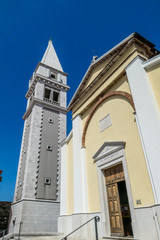 A view on a church and a bell tower from the bottom. The walls of the church are painted yellow, and bell tower's are painted grey. Buildings nicely contrasted with a clear blue sky.