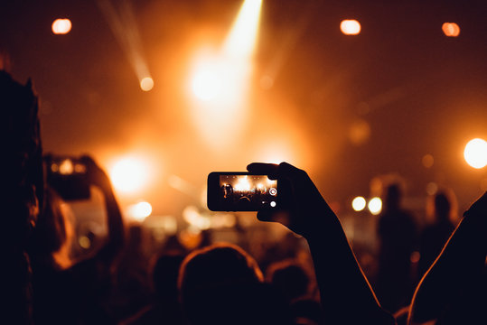 People taking photographs with smart phone during a music concert. Person capturing a video on a mobile phone at a music festival.