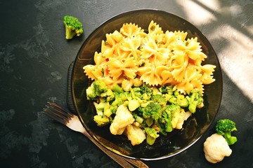 Bow shaped pasta. Pasta and broccoli. Food on a black table background in a glass black plate on a wooden plate. Vegetarian appetizing bright food.