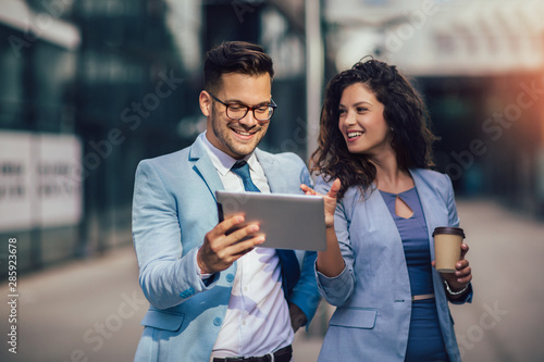 Handsome man and beautiful woman as business partners using digital tablet outdoor