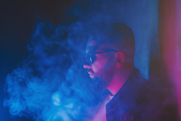 man smokes a cigarette and lets out smoke in a nightclub. 