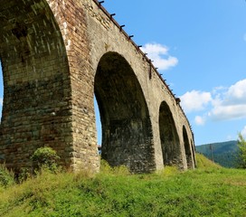 Fototapeta na wymiar Old viaduct bridge on a background of mountains and green grass