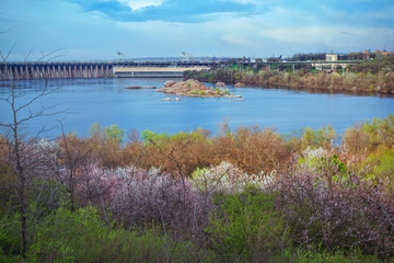 Spring cityscape of  Khortitsa Island  in Zaporizhia, Ukraine – hydroelectric power station on a Dnipro River, cliffs in water, green and blooming trees and blue sky.