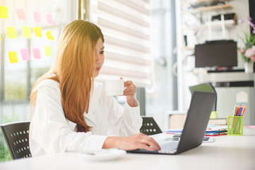 Young woman sitting in coffee shop at White table, drinking coffee and using laptop