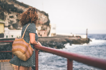 Beautiful curly girl leaning against a railing near the sea looking away in a windy summer evening....