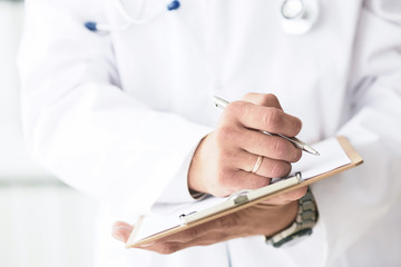 Male doctor in white coat on duty writes information with pen in clipboard close up. Selective focus. Health and medical concept.